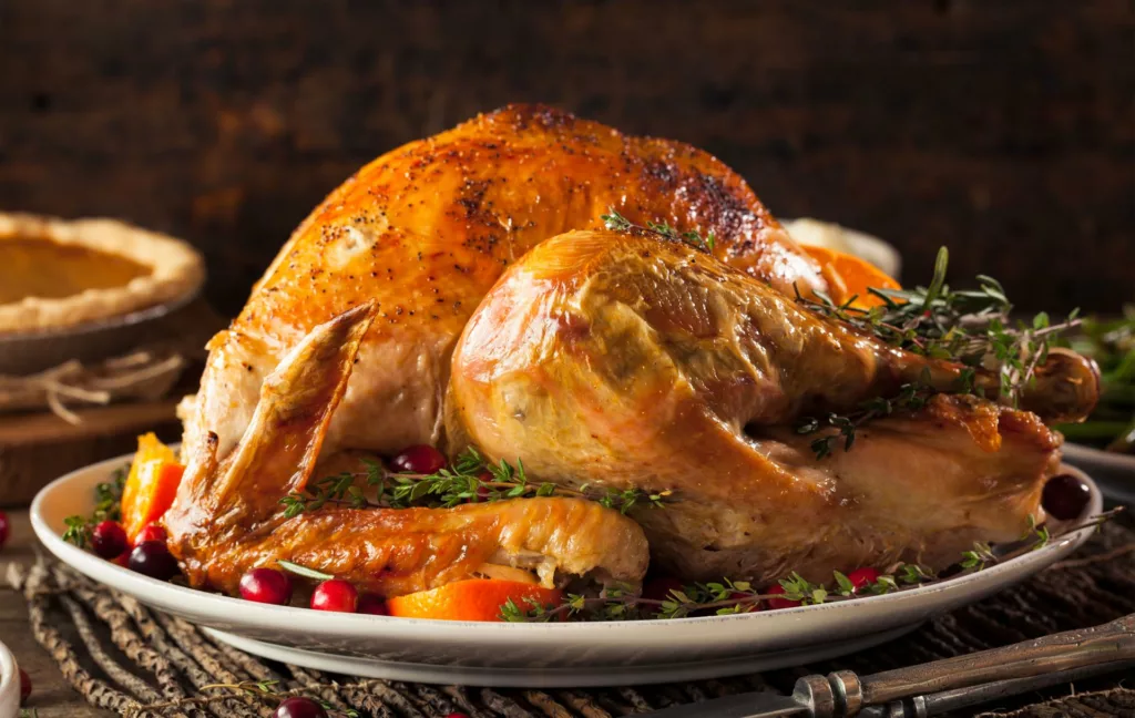 Chapon fermier rôti et doré, servi sur un plat avec herbes de Provence, oranges et cranberries – repas de Noël signé L’Oustau di Galino.